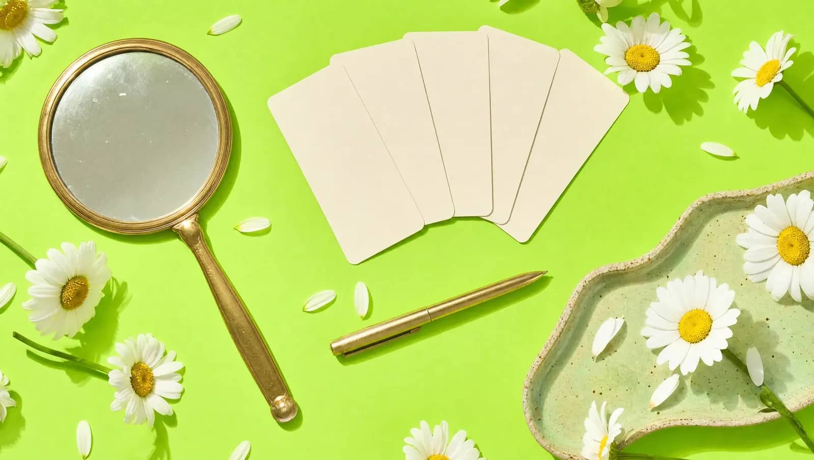 Espelho de mão, cartões em branco em leque, caneta e margaridas sobre fundo verde