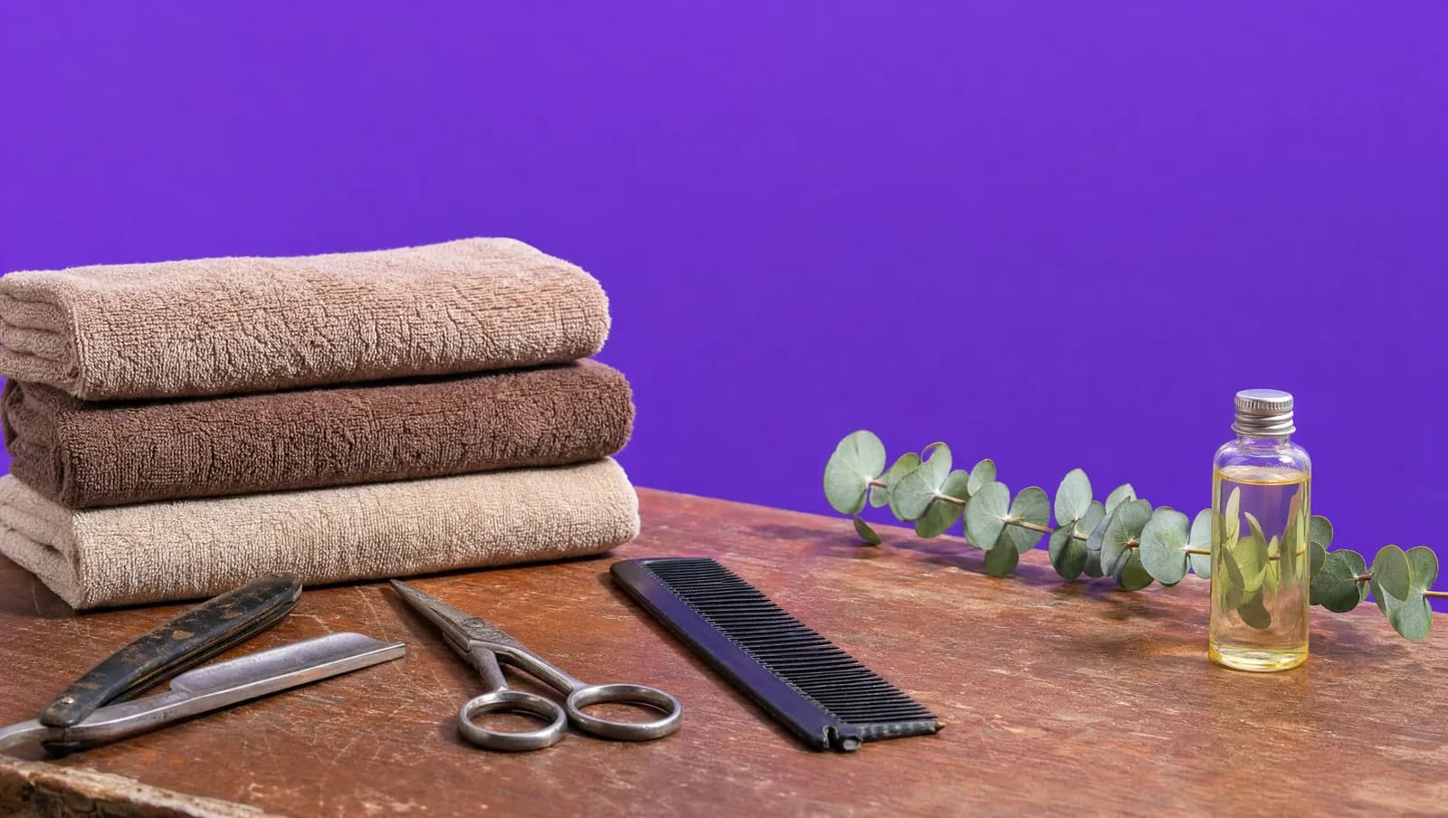 Fotografia de uma bancada de barbearia com navalha, tesoura e toalhas visivelmente usadas, e ao lado um frasco de óleo de massagem ainda lacrado